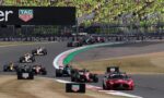 Motor racing scene with a packed grandstand of fans in bright yellow-green shirts; Formula 1 cars on a curving track and a TAG Heuer advertising barrier.
