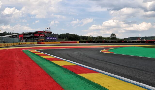 Race track with red, green, yellow, and blue run-off areas and a grandstand in the distance under a cloudy sky