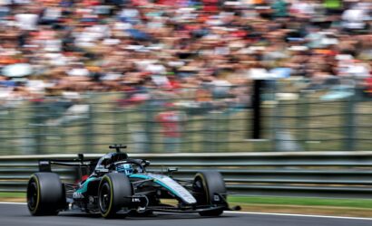 Formula 1 race car (Mercedes) speeding along track with blurred grandstands in the background, capturing high-speed motion.