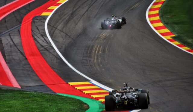 Formula 1 car racing through a sharp left-hand bend on a track with red and yellow curbs and green grass nearby.