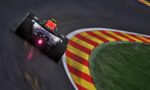 Red Bull racing car speeds around a tight corner on a race track, with red-and-yellow striped curbs to the right.
