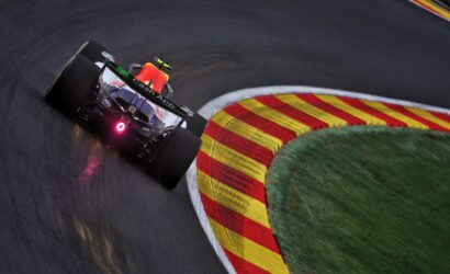 Red Bull racing car speeds around a tight corner on a race track, with red-and-yellow striped curbs to the right.