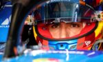 Close-up of a race car drivers face in a colorful helmet; eyes visible through the visor with Barclays and Atlassian logos nearby.