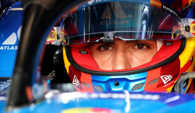 Close-up of a race car drivers face in a colorful helmet; eyes visible through the visor with Barclays and Atlassian logos nearby.