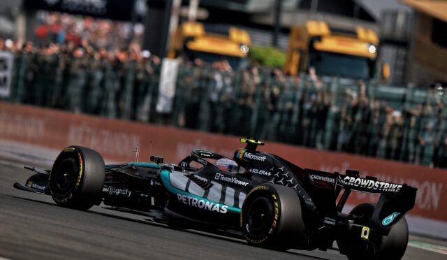 Formula 1 race car labeled Petronas and Microsoft speeding along a race track with a blurred crowd in the background.