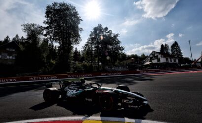 Formula 1 car on a race track with Moët & Chandon banners along the barriers under a bright sun in the sky.