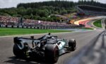 Formula 1 car on a race track turning, with crowded grandstands and forested hills in the background