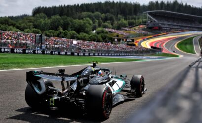 Formula 1 car on a race track turning, with crowded grandstands and forested hills in the background