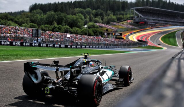 Formula 1 car on a race track turning, with crowded grandstands and forested hills in the background