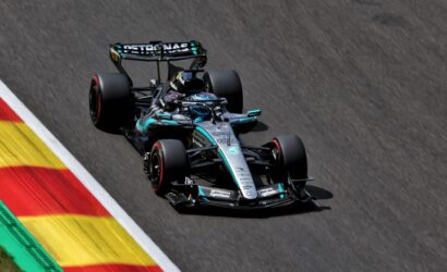 Mercedes‑AMG Petronas Formula 1 car speeding along a race track beside red‑yellow curbs.
