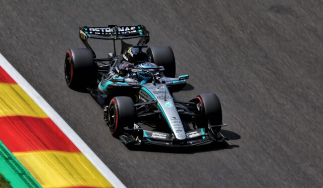 Mercedes‑AMG Petronas Formula 1 car speeding along a race track beside red‑yellow curbs.