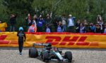 Formula 1 car on a gravel pit area with photographers behind a safety fence taking pictures of the scene at a race event