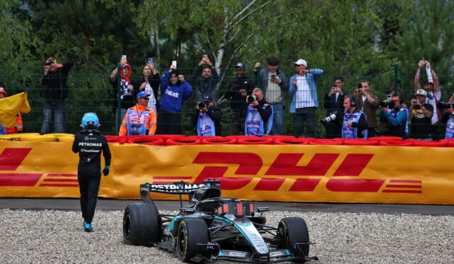 Formula 1 car on a gravel pit area with photographers behind a safety fence taking pictures of the scene at a race event