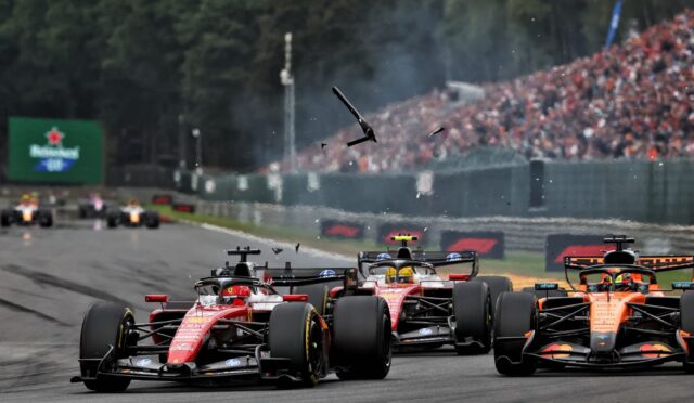 Formula 1 cars race down the straight with a packed grandstand in the background; debris or parts soar through the air above the track.