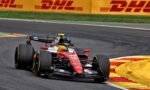 Red Formula 1 car rounding a bend on a race track, with yellow-red curbs and DHL banners in the background.