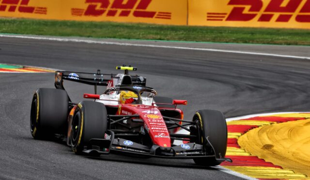 Red Formula 1 car rounding a bend on a race track, with yellow-red curbs and DHL banners in the background.