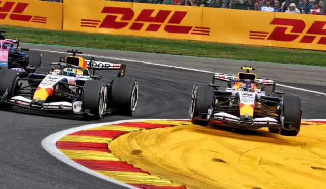 Formula 1 race cars cornering through a chicane with DHL barriers and a cheering crowd in the background.