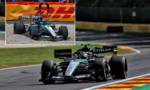 Mercedes F1 car on a race track navigating a left-handed curve, with a red-yellow advertising barrier in the background.