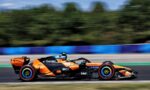 Orange Formula 1 race car speeding along a track, sponsor decals visible along the body with a blurred background for motion.