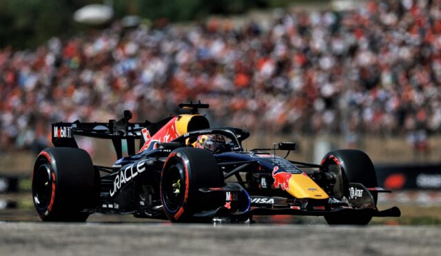 Red Bull Racing Formula 1 car speeds along the track with a large blurred crowd in the background.