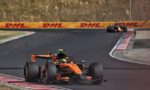 Orange Formula 1 car on a curving race track with DHL barriers in the background