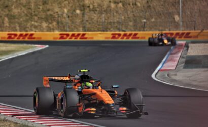 Orange Formula 1 car on a curving race track with DHL barriers in the background