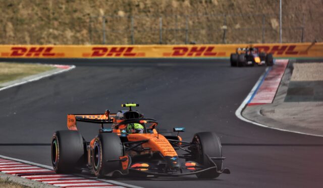 Orange Formula 1 car on a curving race track with DHL barriers in the background