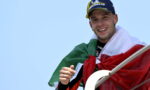 Smiling man wrapped in the Italian flag, wearing a blue Michelin cap, against a clear blue sky.