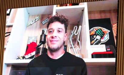 Smiling man in a black shirt standing in a room with shelves, trophies, and decorative items behind him.