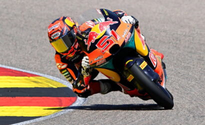 Racing motorcyclist in orange suit leaning into a corner on a track, bike adorned with Red Bull livery and number 01.