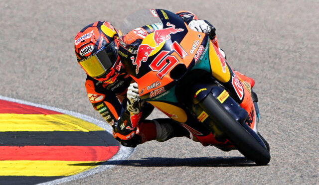 Racing motorcyclist in orange suit leaning into a corner on a track, bike adorned with Red Bull livery and number 01.