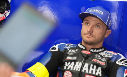 Motorcycle racer in Yamaha gear sitting against a blue wall, looking upward in thought.