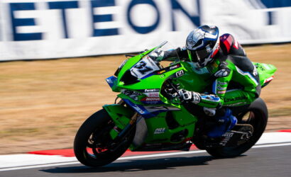 Moto racer on a green Kawasaki sportbike leaning into a turn on a race track with number 34 on the bike and a blurred background.