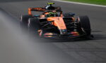 Orange Red Bull Formula 1 car speeds along a race track, front view with driver helmet visible in cockpit and blurred foreground