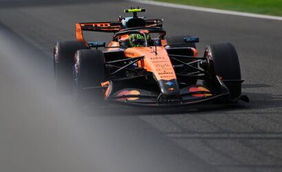 Orange Red Bull Formula 1 car speeds along a race track, front view with driver helmet visible in cockpit and blurred foreground