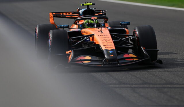 Orange Red Bull Formula 1 car speeds along a race track, front view with driver helmet visible in cockpit and blurred foreground