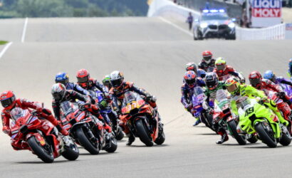 Group of motorcycle racers leaning into a turn on a sunny track during a race in close formation.