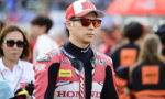 MotoGP rider in a red Honda racing suit and cap with the number 30, wearing orange sunglasses in the paddock setting