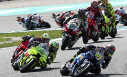Group of motorcycle racers leaning into a tight turn on a racetrack, neon green bike leading the pack and blue bike close beside.
