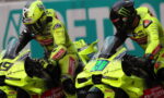 Two neon-yellow racing motorcycles with riders leaning forward side by side on a track, both in matching fluorescent gear and helmets.