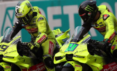 Two neon-yellow racing motorcycles with riders leaning forward side by side on a track, both in matching fluorescent gear and helmets.