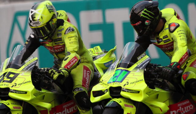 Two neon-yellow racing motorcycles with riders leaning forward side by side on a track, both in matching fluorescent gear and helmets.