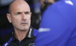 Head-and-shoulders of a bald man in a blue-and-black Yamaha polo, looking serious in a team pit area