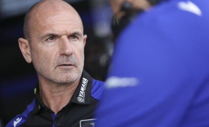 Head-and-shoulders of a bald man in a blue-and-black Yamaha polo, looking serious in a team pit area