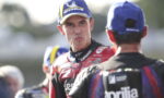 MotoGP rider in red Lenovo suit making a funny face toward another rider wearing a blue cap.