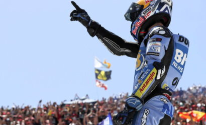 Motocross rider in blue gear raises a gloved fist in celebration as a large cheering crowd watches. Ninth image shows sponsor logos like Red Bull on the helmet and suit.