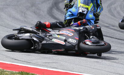 Motorcycle racer slides on the track during a corner, another blue bike close behind on the racing line.