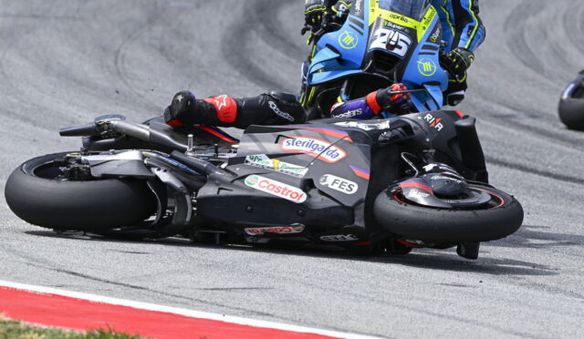 Motorcycle racer slides on the track during a corner, another blue bike close behind on the racing line.