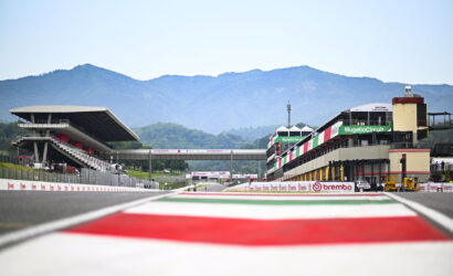Race track at Mugello Circuit with grandstands and pit complex, mountains in background.
