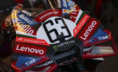 Close-up of a racing motorcycle fairing covered in sponsor decals including Lenovo, Frecciarossa, Tim, and Monster Energy on a dark carbon background on red/blue accents